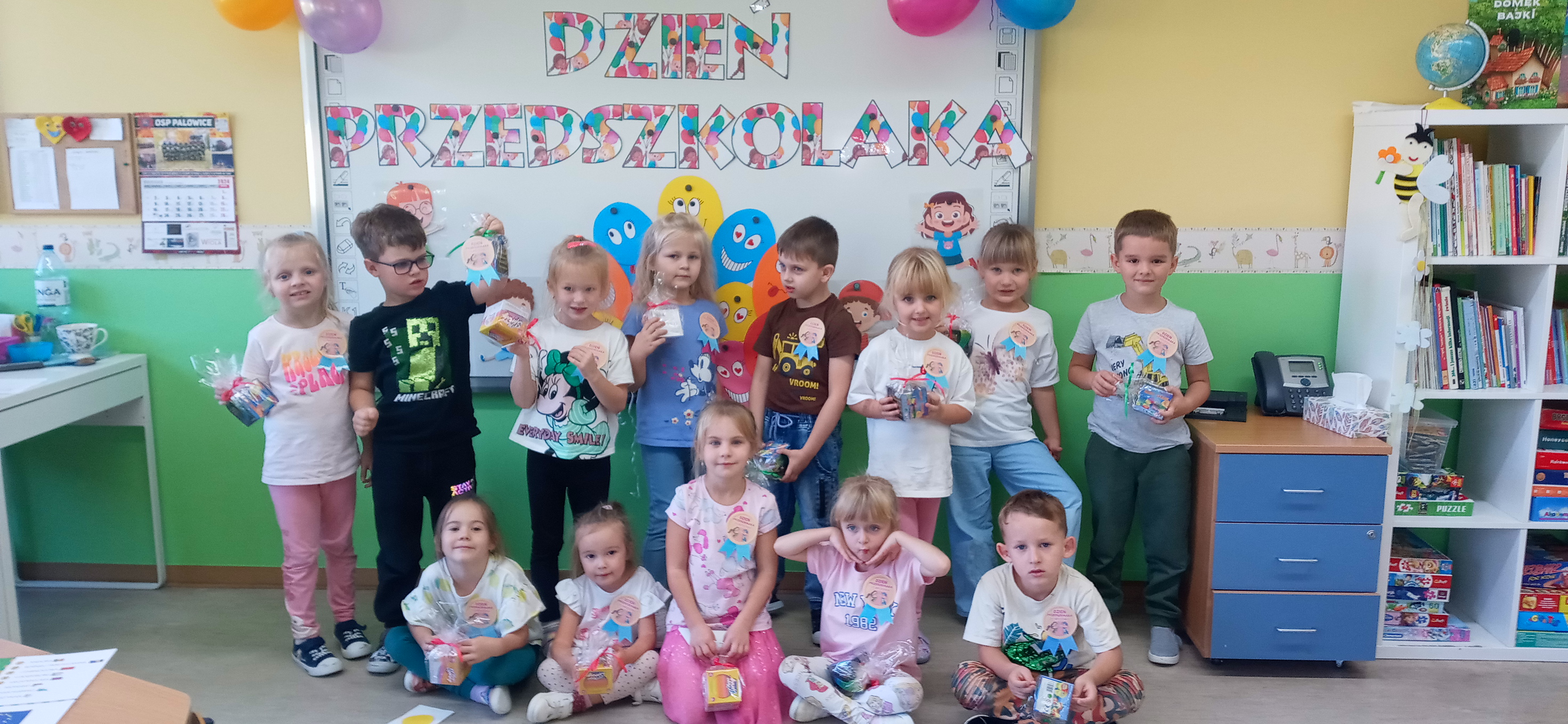 Grupa dzieci stoi  pod napisem Dzień Przedszkolaka w rękach trzymając upominki.